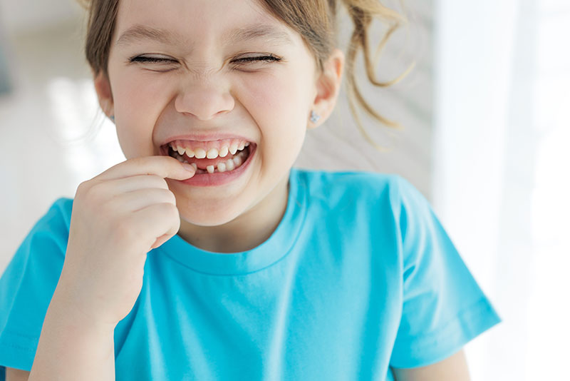 Kleines Mädchen zeigt beim Zahnarzt lachend auf seinen ausgefallenen Schneidezahn